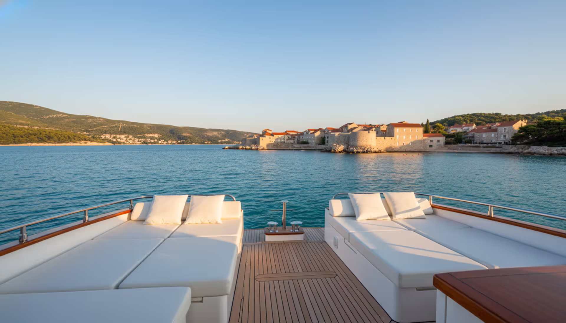 Luxury yacht stern view overlooking turquoise Adriatic Sea with Dalmatian coast medieval stone town and green hills in background
