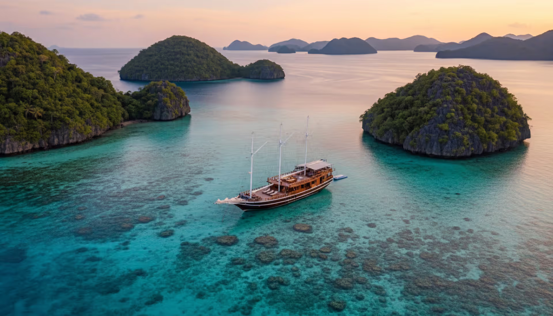 Luxury wooden phinisi sailing yacht anchored in turquoise lagoon among karst limestone islands in Raja Ampat Indonesia at sunset aerial drone view