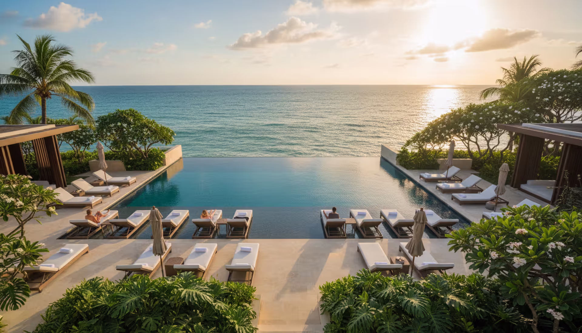 Aerial view of a luxury infinity pool overlooking the ocean at an adults-only resort with white lounge chairs and tropical greenery