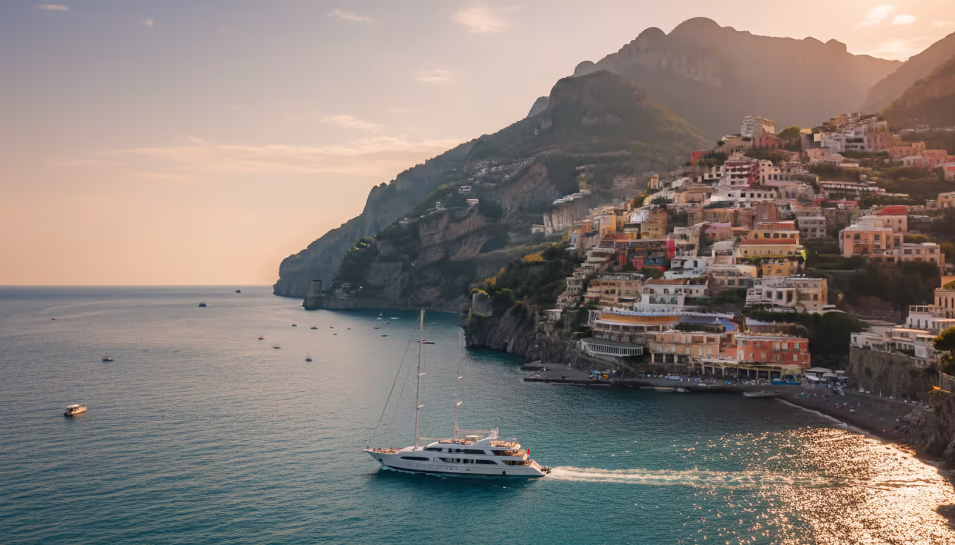 Panoramic view of Amalfi Coast with colorful cliffside houses, turquoise sea, and a luxury white yacht at golden hour