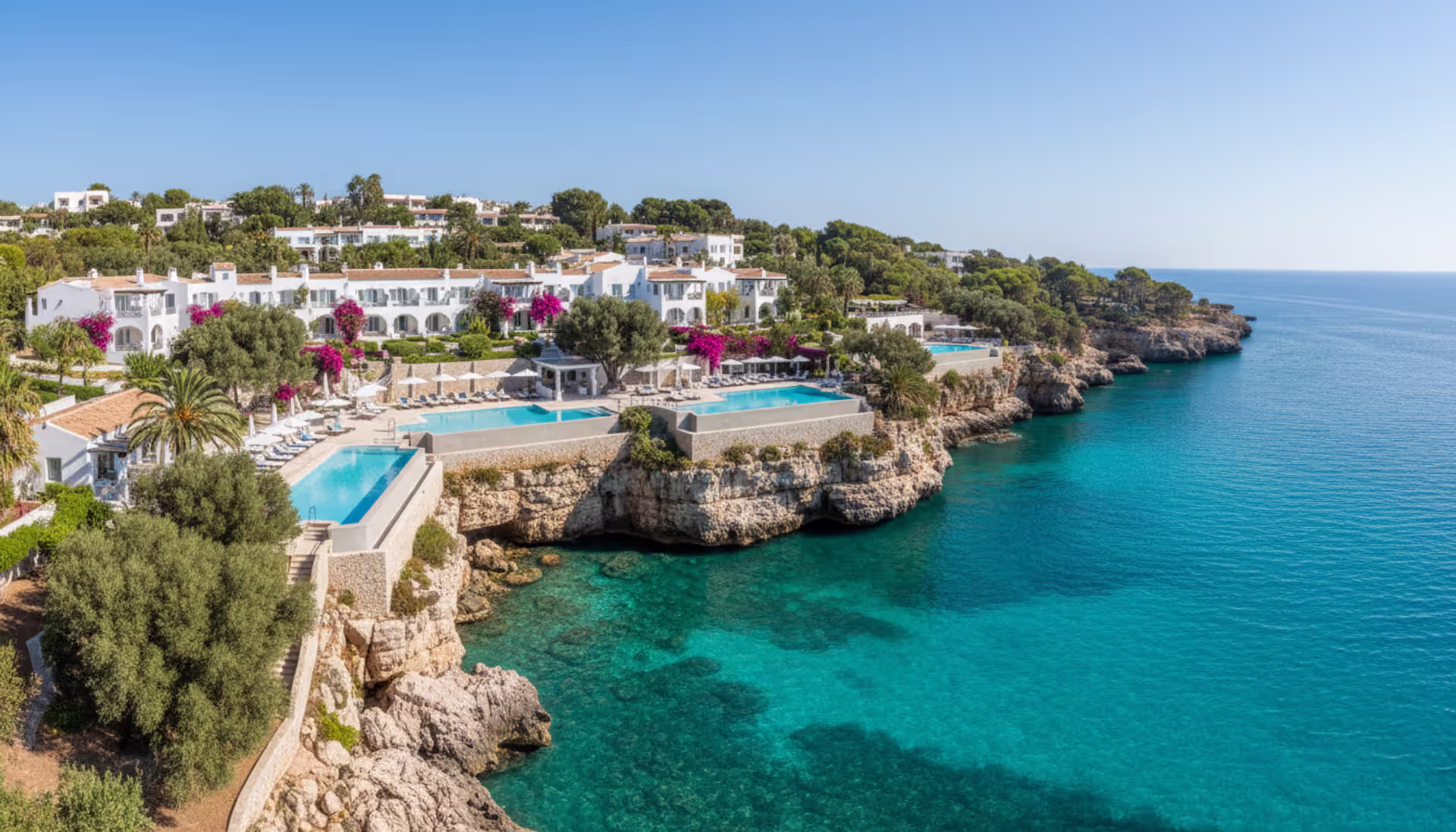 Panoramic view of a Mediterranean cliffside luxury spa resort with infinity pool overlooking turquoise sea waters and olive groves