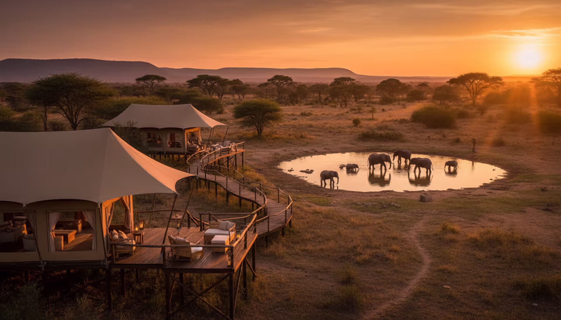 Luxury safari lodge with canvas tents overlooking a waterhole where elephants gather at sunset in the African savannah