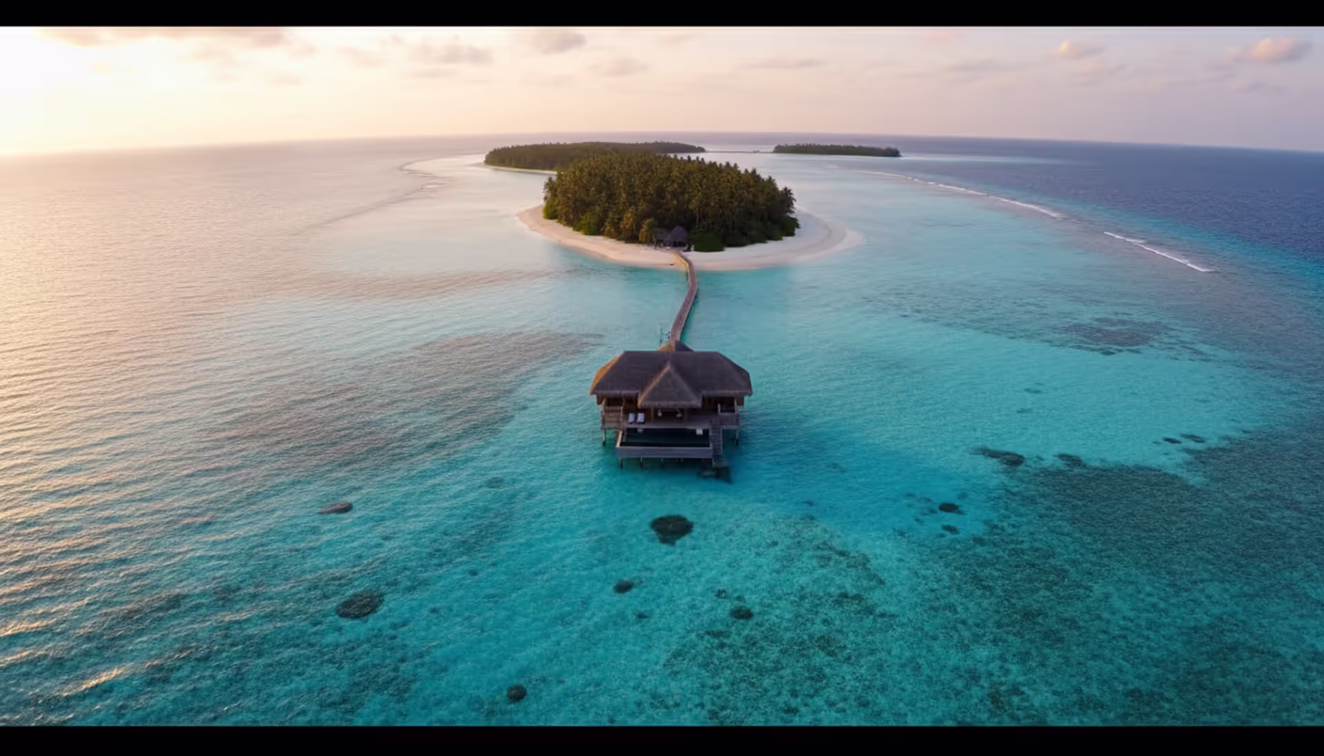 Aerial view of a single overwater bungalow in the turquoise Maldives ocean near a tropical palm island at golden sunset