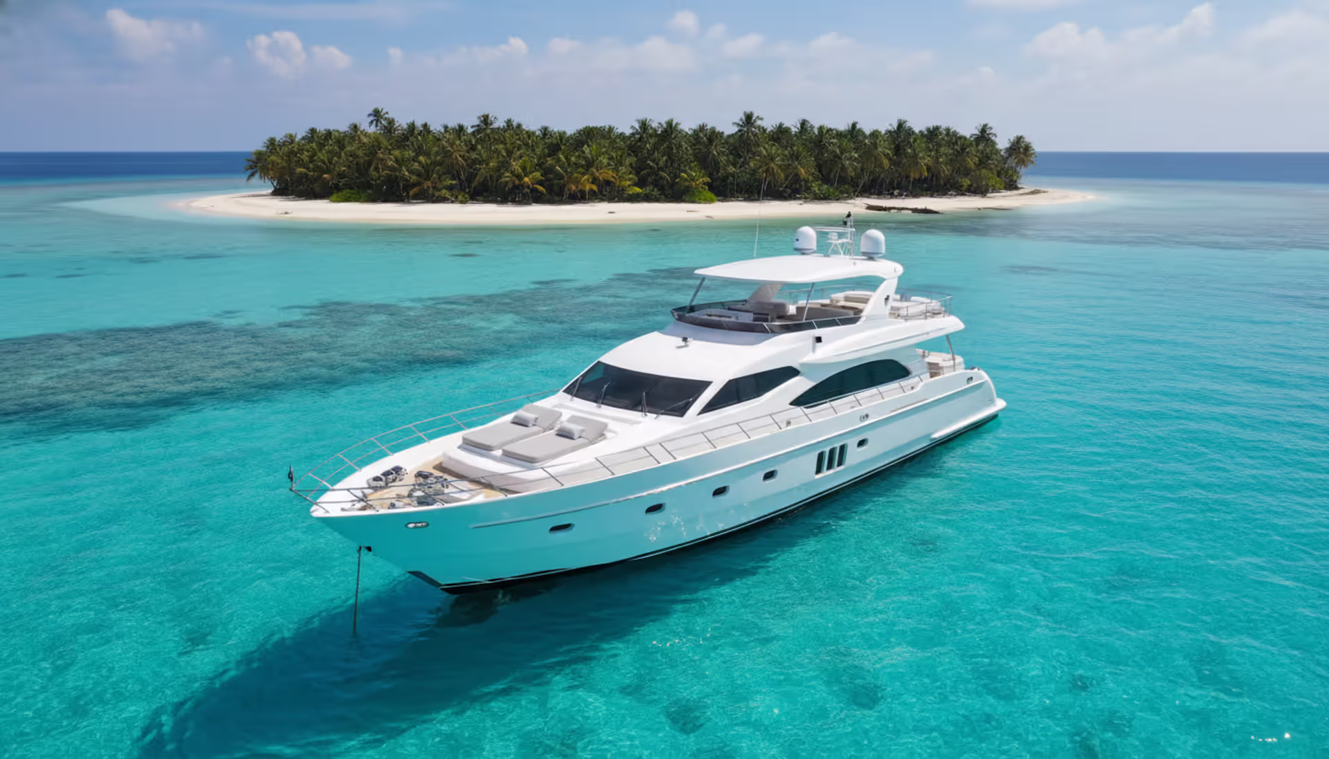 Luxury white motor yacht anchored near a tropical island with turquoise water and palm trees, aerial view
